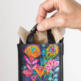 Hand holding a small black bag with colorful floral designs on a light gray background