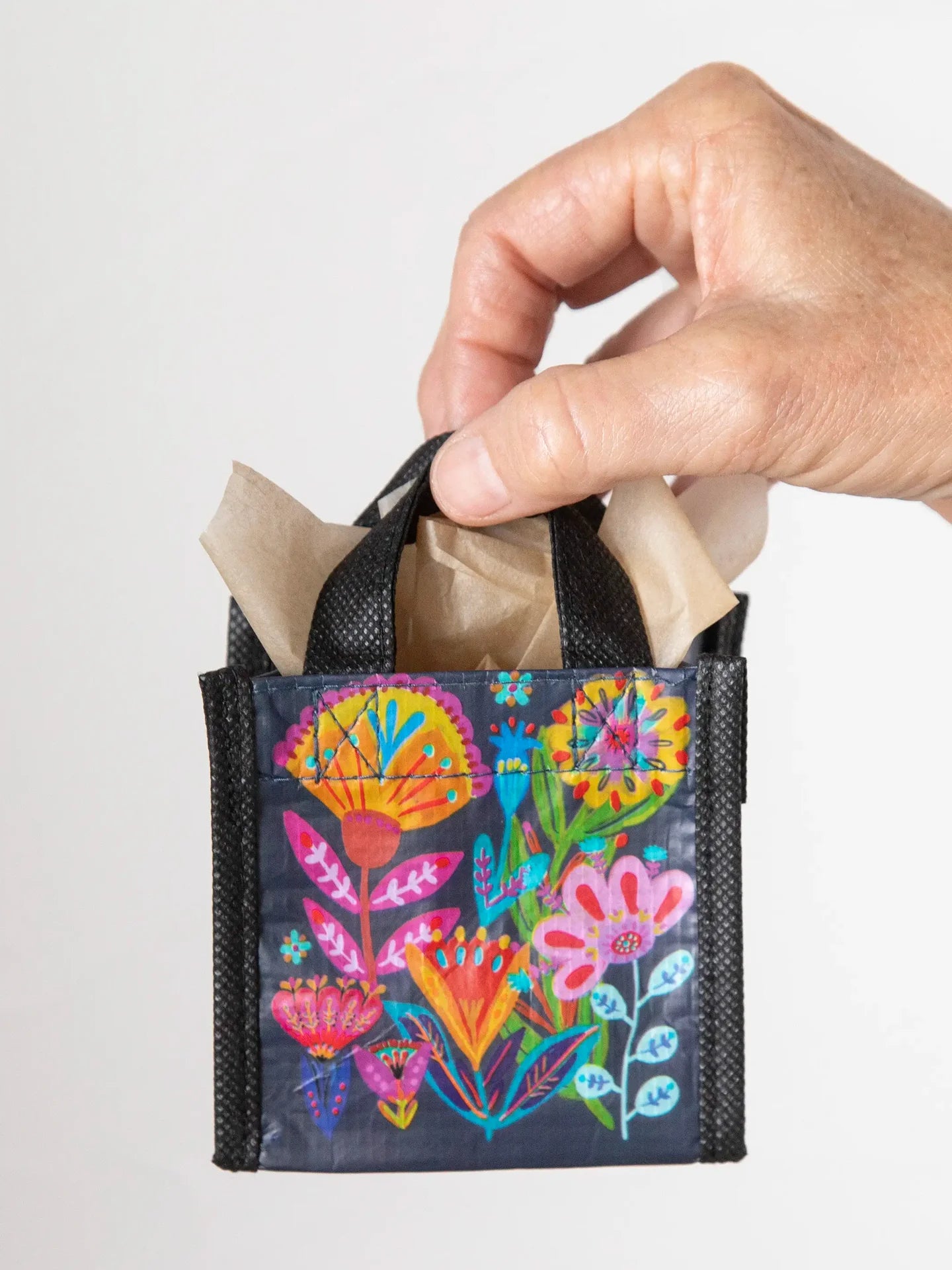 Hand holding a small black bag with colorful floral designs on a light gray background