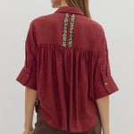 Woman wearing a burgundy shirt with decorative back panel on a plain background