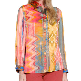 Woman wearing a colorful patterned blouse with sheer sleeves on a white background