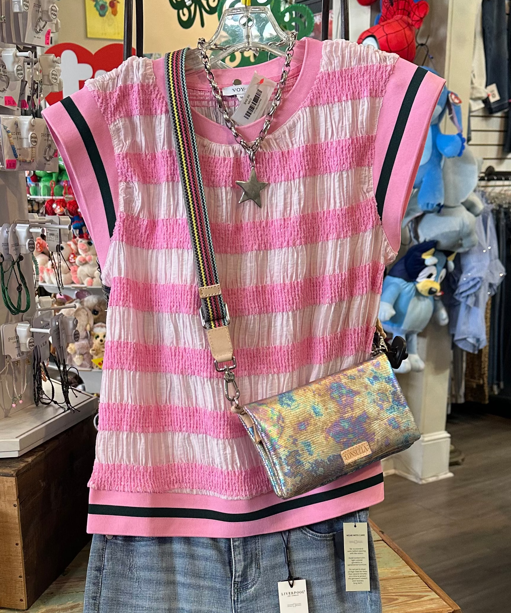 Pink striped shirt, jeans, and colorful bag on a mannequin in a store setting.