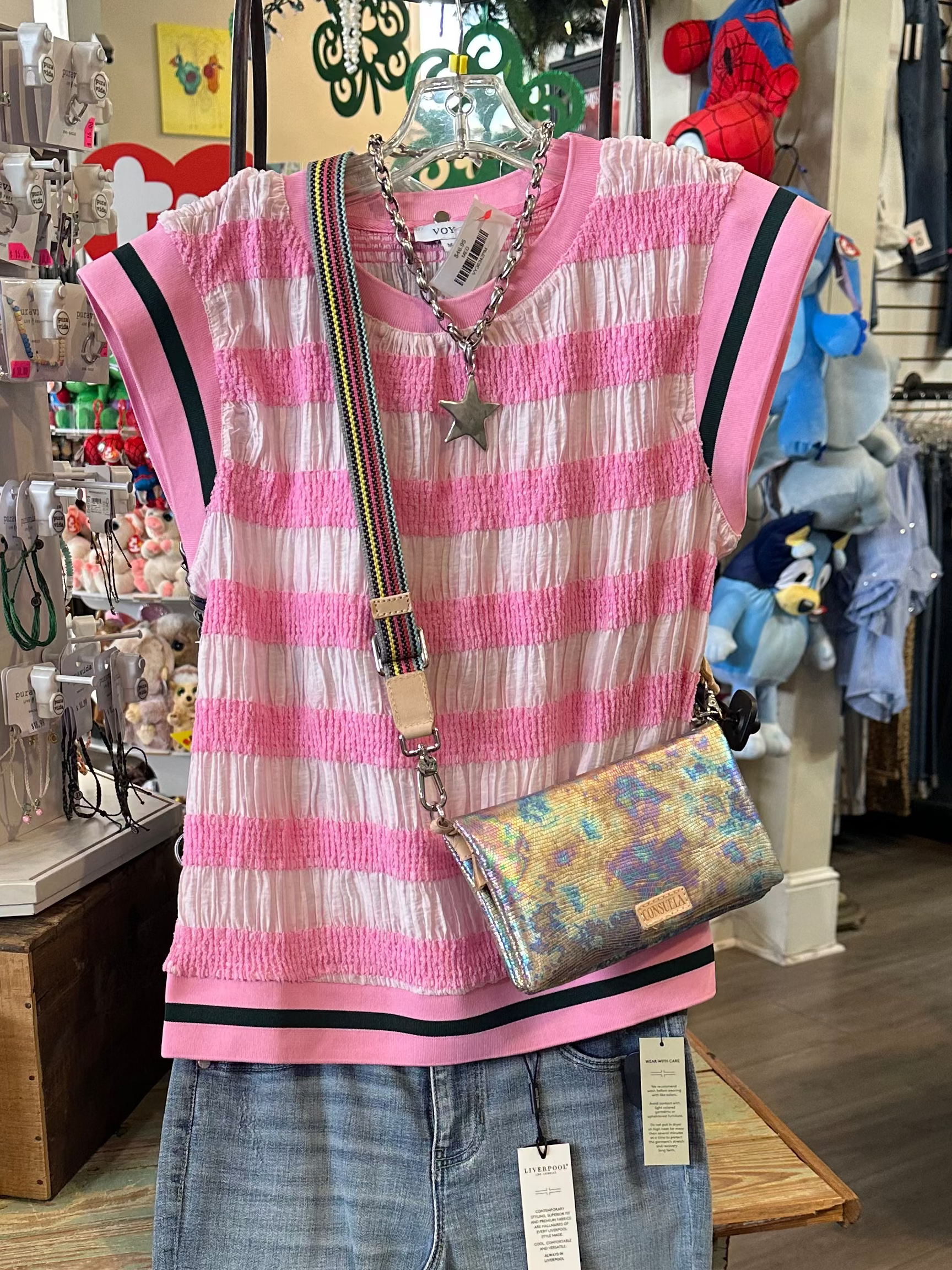 Pink striped shirt, jeans, and colorful bag on a mannequin in a store setting.