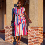 Woman in a colorful dress standing between two stone columns with a building in the background.