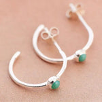 Silver earrings with green gemstones on a beige background