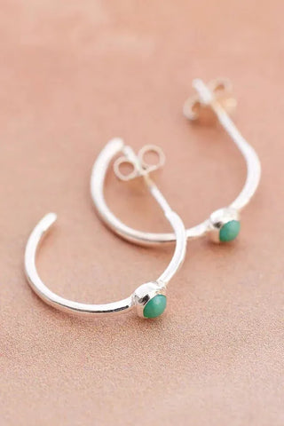 Silver earrings with green gemstones on a beige background