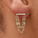 Gold chain earring worn on a person's ear with a blurred background