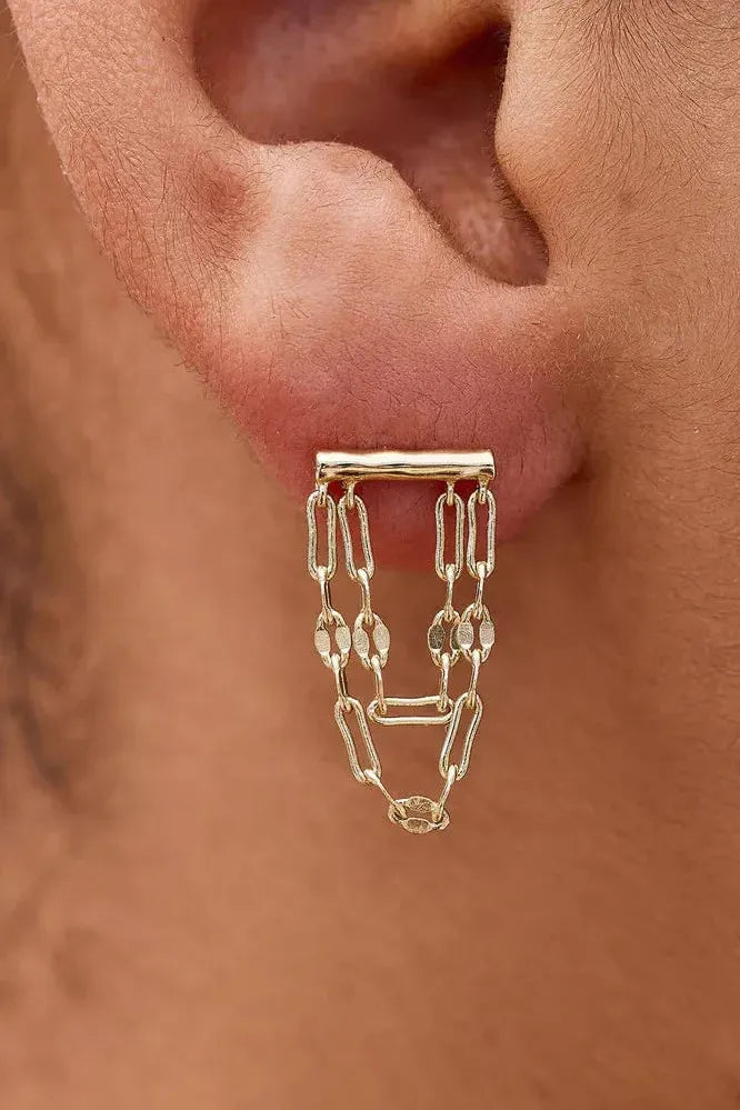 Gold chain earring worn on a person's ear with a blurred background