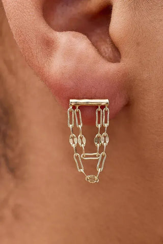 Gold chain earring worn on a person's ear with a blurred background