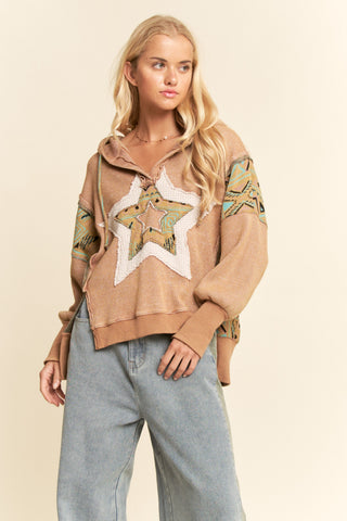 Woman wearing a beige hoodie with floral patterns and light blue jeans on a beige background
