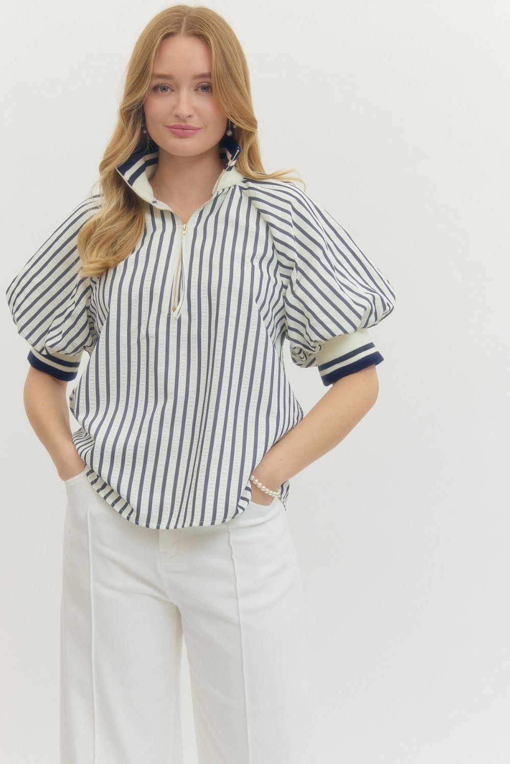 Woman wearing a striped shirt and white pants on a plain background