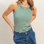 Woman wearing a green and white striped tank top and blue denim shorts on a plain background