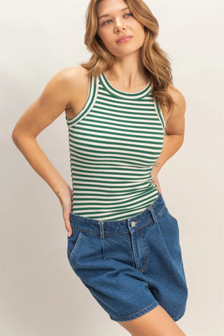 Woman wearing a green and white striped tank top and blue denim shorts on a plain background