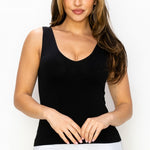 Woman wearing a black tank top and white pants on a plain background
