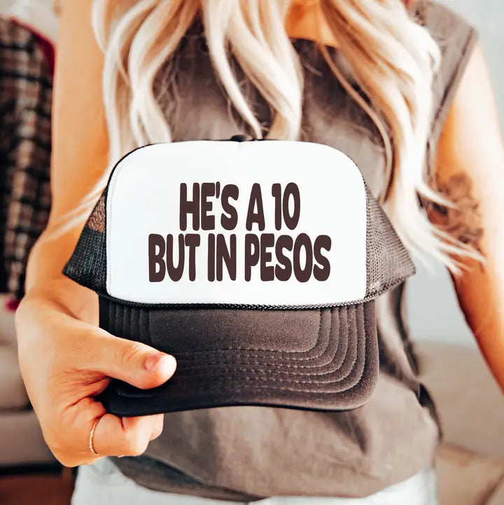 Person holding a cap with text 'HE'S A 10 BUT IN PESOS' on a blurred background