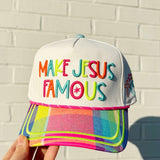 Colorful cap with 'MAKE JESUS FAMOUS' text against a light brick wall.
