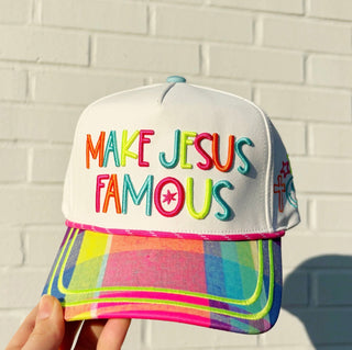 Colorful cap with 'MAKE JESUS FAMOUS' text against a light brick wall.