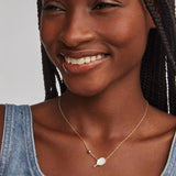 Woman wearing a gold necklace with a pendant against a neutral background