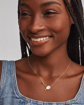 Woman wearing a gold necklace with a pendant against a neutral background