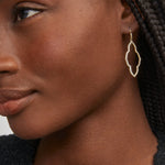 Close-up of a woman wearing gold hoop earrings with a neutral background