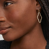 Close-up of a woman wearing gold hoop earrings with a neutral background