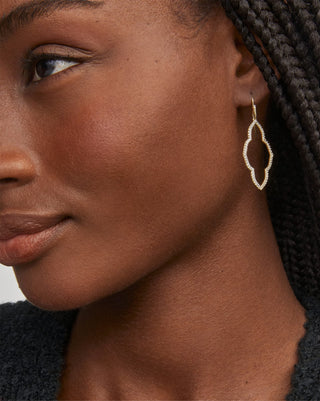 Close-up of a woman wearing gold hoop earrings with a neutral background