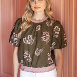 Woman wearing a floral blouse and white shorts in front of pink cabinets.