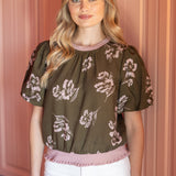 Woman wearing a floral blouse and white shorts in front of pink cabinets.