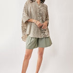 Woman wearing a leopard print top and green shorts on a white background