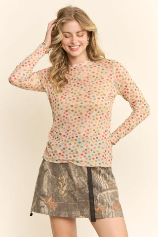 Woman wearing a colorful polka dot top and patterned skirt on a plain background