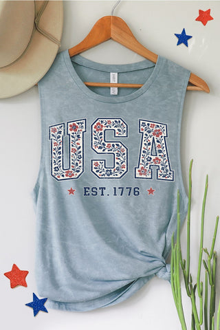 Blue tank top with 'USA EST. 1776' design on a hanger against a white wall.
