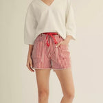 Woman wearing a white top and red striped shorts on a beige background