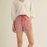 Woman wearing a white top and red striped shorts on a beige background
