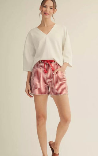 Woman wearing a white top and red striped shorts on a beige background
