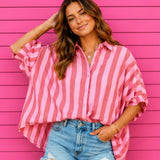 Woman wearing a pink and white striped shirt over a blue denim shirt against a pink wooden background