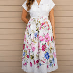 Woman wearing a white blouse with a floral skirt against a beige wall.