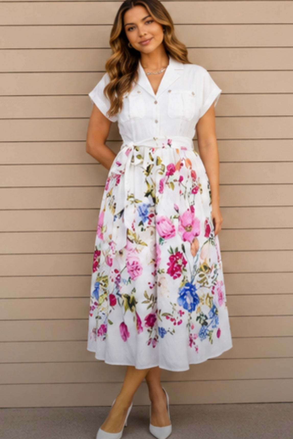 Woman wearing a white blouse with a floral skirt against a beige wall.