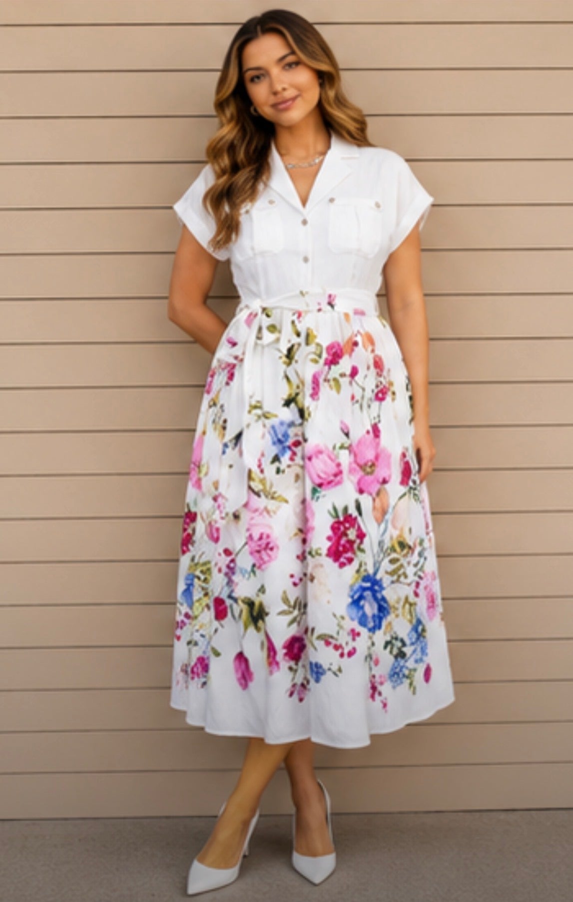 Woman wearing a white blouse with a floral skirt against a beige wall.