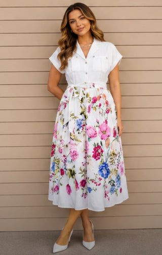 Woman wearing a white blouse with a floral skirt against a beige wall.