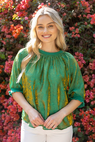 Woman wearing a green blouse with yellow patterns in front of pink flowers
