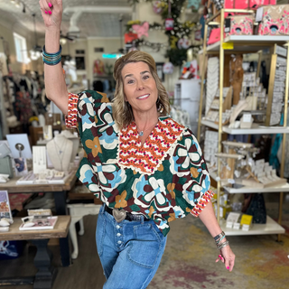 Woman in a colorful shirt and jeans pointing upwards in a store.