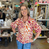 Woman in a store wearing a colorful shirt and blue jeans, smiling.