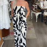 Woman in a black and white patterned jumpsuit standing in a store with various items on display.
