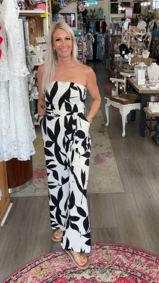 Woman in a black and white patterned jumpsuit standing in a store with various items on display.
