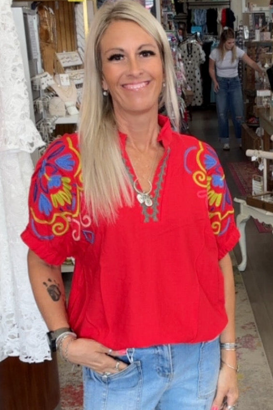 Woman in a red blouse with colorful patterns standing in a store.
