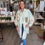Woman standing in a store wearing a floral kimono-style jacket.
