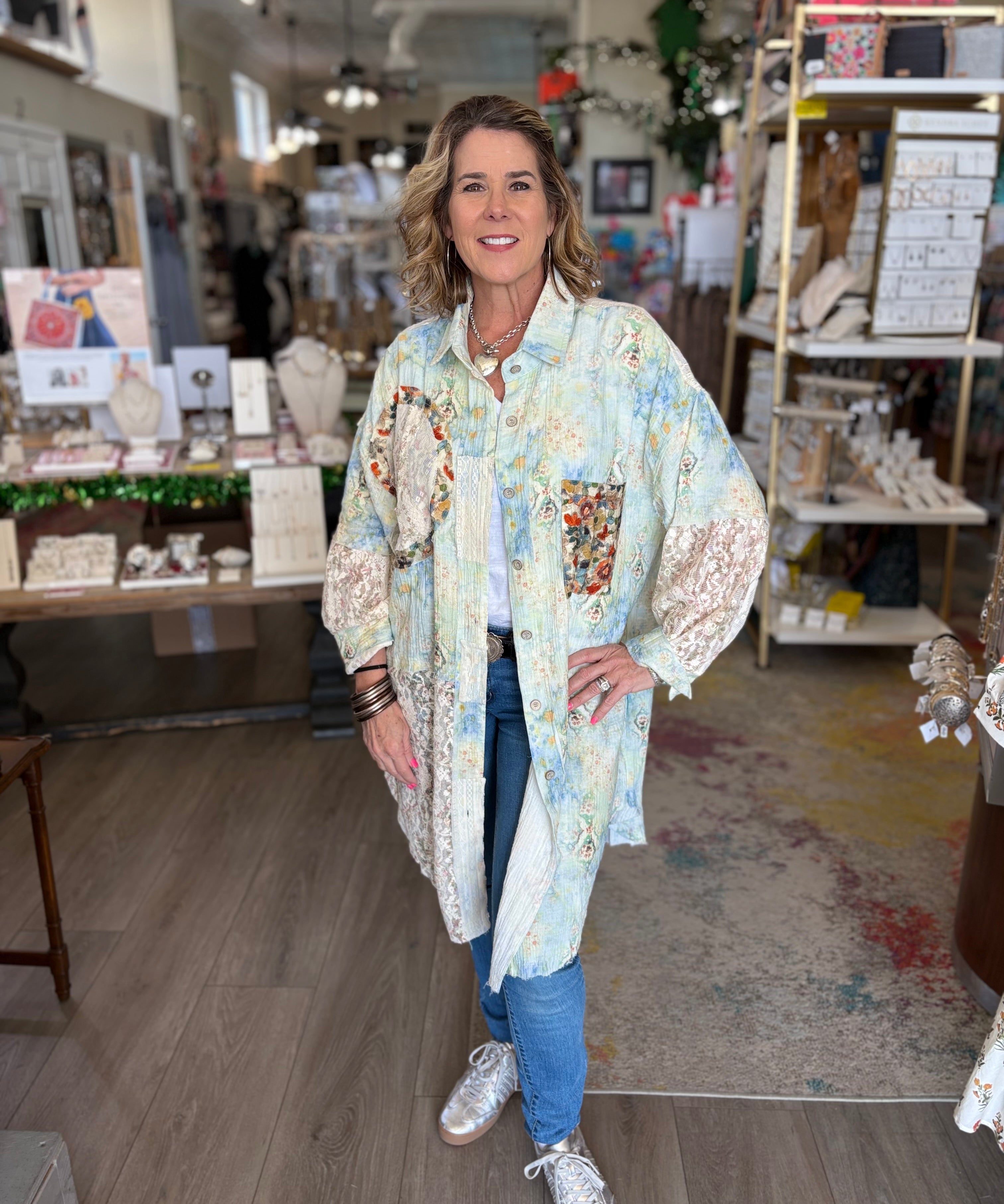 Woman standing in a store wearing a floral kimono-style jacket.