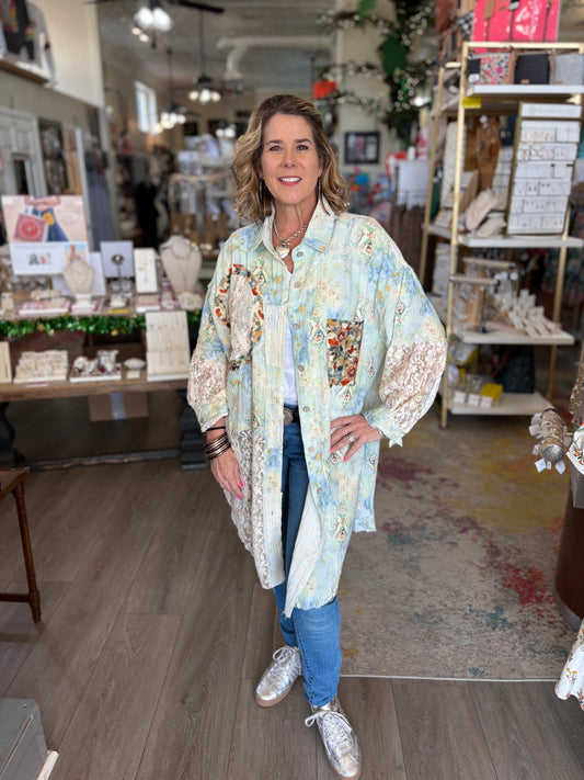 Woman standing in a store wearing a floral kimono-style jacket.