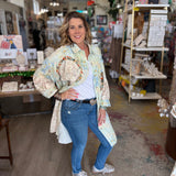 Woman standing in a store holding a decorative item, wearing a floral jacket and blue jeans.
