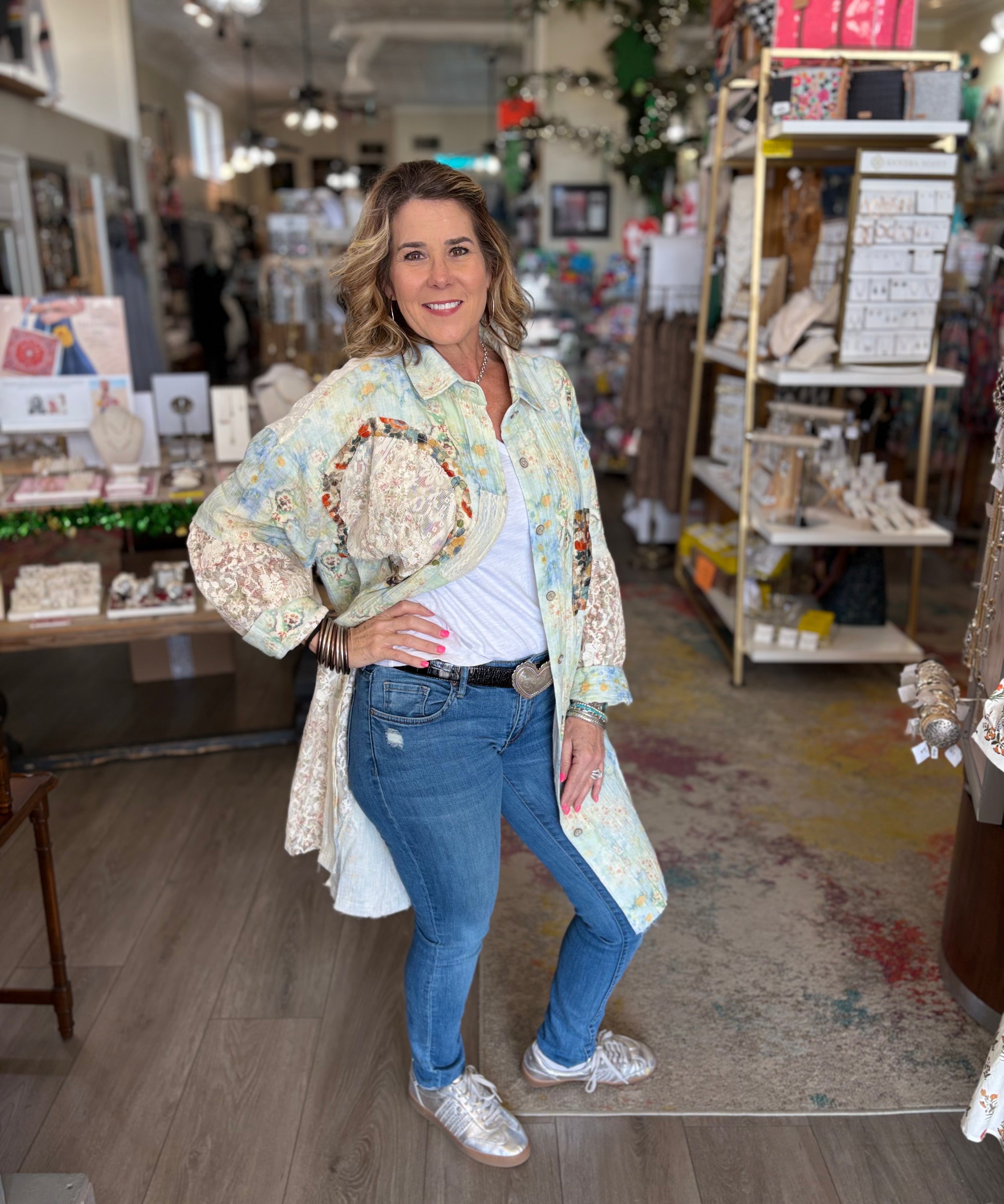 Woman standing in a store holding a decorative item, wearing a floral jacket and blue jeans.