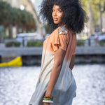 Woman in a light dress holding a handbag by a waterfront with blurred background